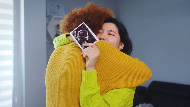 Multiracial lesbian couple expecting baby. Embracing with ultrasound baby picture. Maternity support. High quality photo