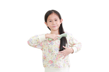 Smiling asian little kid girl combing long hair on white. Hair care concept