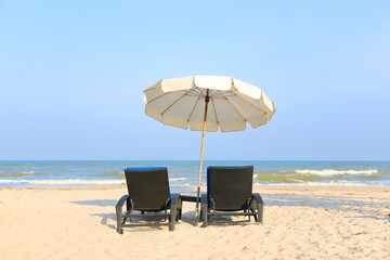 Beach chairs on the sand beach with white umbrella on cloudy blue sky and sun