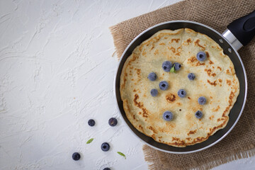 Pancake in a pan with blueberry and a light background.