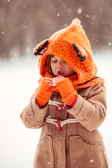 Frozen Caucasian girl child in a coat and a knitted hat, a fox cub walks through a snowy park,...