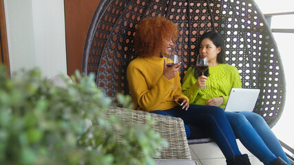 Two woman gossiping in the swing. Lesbian couple browsing social media on the laptop with red wine. High quality photo