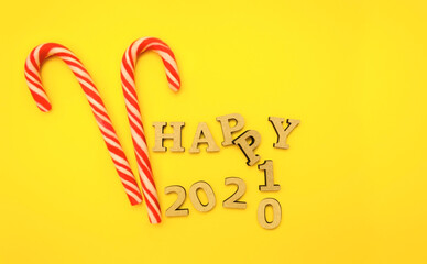 Coming of Happy New Year 2021. Wooden letters in a New Year's cap on a yellow background with red candies, gingerbread. Festive decoration or postcard concept. Top view and flat. Copy space