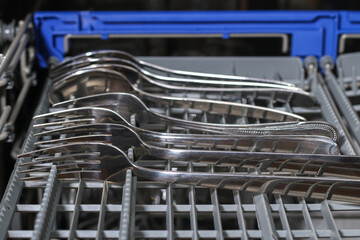 A man loads dirty dishes, plates, spoons, forks, cutlery into dishwasher tray.