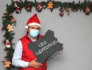 Latino man with protection mask, Santa Claus hat and blackboard with message 