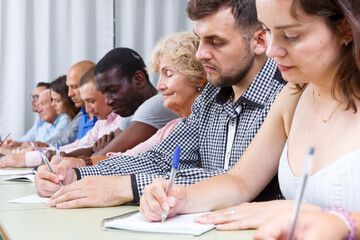 Group people mixed age listening and writing during business course.