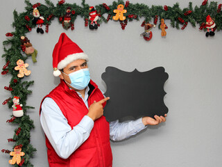 latin man with protection mask and blackboard to write message, in christmas decoration, new normal...