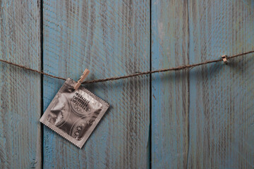 A condom in package hanging on the rope against blue wooden rustic background. Copyspace. Concept of love, Saint Valentine's Day