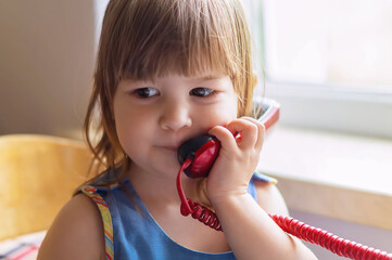 Portrait of a cute little girl talking on an old home phone. Communication, the concept of relationships. European children.