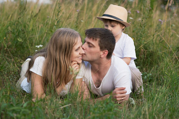 Happy family lying in grass and enjoying walk together at meadow in summer