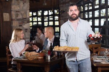 Positive male waiter welcoming guests to country restaurant. High quality photo