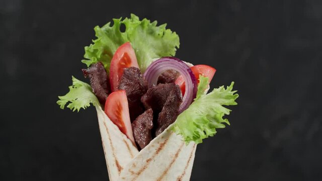 Shawarma or doner kebab moves on an black background. Shawarma is made with tortilla, beef, tomato, onion and lettuce.