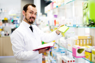 Smiling man pharmacist checking assortment of drugs in pharmacy