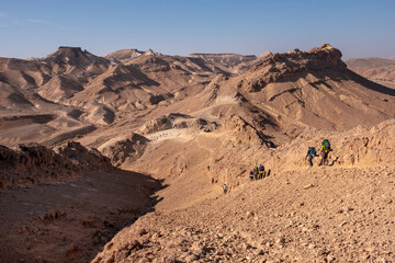 Hikers on a hiking trail in a remote desert region. Panoramic desert landscape of colorful sandy hills, dry wadies, rock formations and boulders.