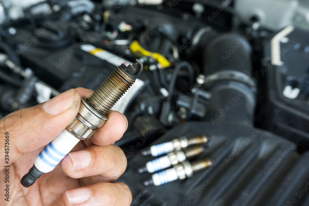 Wall mural hand of the auto mechanic holding the old spark plug on blurred engine car on background.