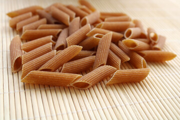Whole wheat uncooked pasta on a wooden background