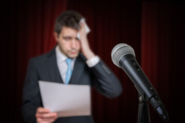 Nervous speaker is afraid of public speech and is sweating. Microphone in front.