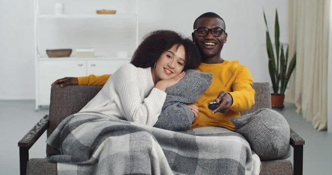 Loving couple boyfriend and girlfriend husband and wife newlyweds sitting together on couch at home in living room cuddling watching TV television movies online on internet spend time together on sofa