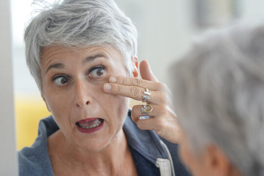 Mature White-haired Woman Checking Eye Wrinkles In Front Of Mirror