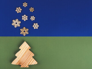 The zero waste new year concept as a handmade wooden conifer tree and falling wooden snowflakes with copyspace on the blue and green background.