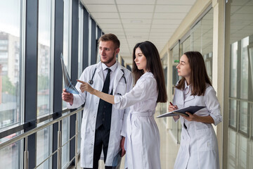 Three young doctors discusses the results of an MRI scan of the patient's head in modern hospital hallway.
