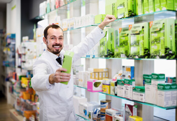 Naklejka na ściany i meble Smiling man pharmacist showing right drug in drugstore