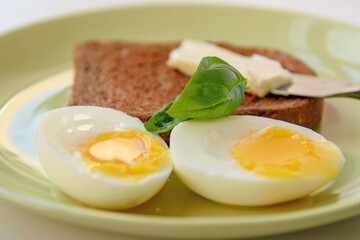 Two soft-boiled egg halves on a plate. Basil leaf, toast and butter. Close up.