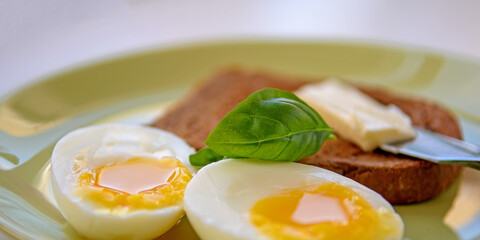 Two soft-boiled egg halves on a plate. Basil leaf, toast and butter. Close up.