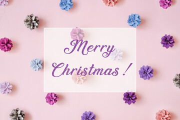 Fototapeta na wymiar Multi-colored Christmas tree cones pattern on pink background. Merry Christmas lettering. Flat lay style.