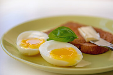Two soft-boiled egg halves on a plate. Basil leaf, toast and butter. Close up.