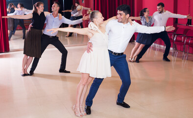 Young positive people dancing samba in pairs in dance hall