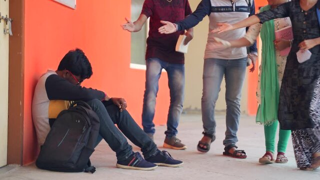 Concept of college bullying at university campus - group of students coming and hitting, abusing to sad boy while sat in corridor