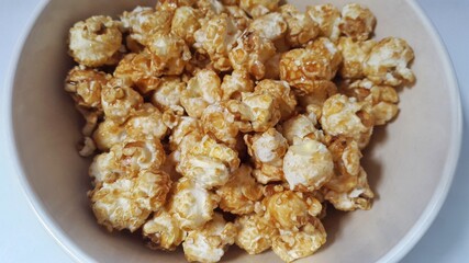 Caramel popcorn in bowl isolated on white background. Popcorn (popped corn, popcorns or pop-corn) is a variety of corn kernel which expands and puffs up when heated.
