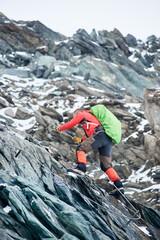 Brave alpinist holding rope while climbing alpine ridge. Young climber with backpack ascending mountain and trying to reach mountaintop. Concept of mountaineering, alpinism and alpine climbing.