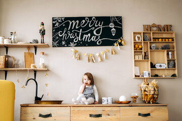 Beautiful blonde girl in waiting for Merry Christmas playing in a cozy kitchen at home