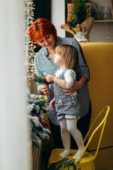 Beautiful blonde girl with grandmother in waiting for Merry Christmas playing in a cozy kitchen at home