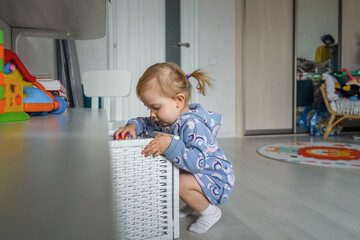 Adorable little girl in beautiful suit at home, near box with toys. Light and white interior.