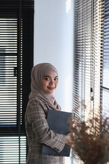 Portrait of muslim businesswoman in hijab is holding document and standing in office room.