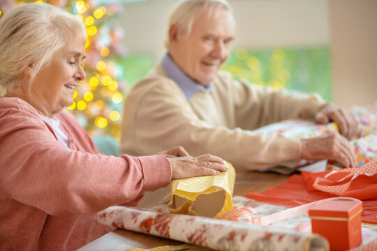 Elderly Couple Packing Christmas Gifts And Looking Contented