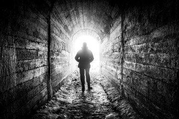 The man walks down the tunnel towards the light.