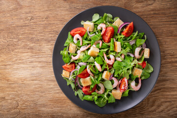 plate of fresh salad with shrimps, greens and tomato on a wooden table