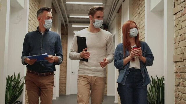 Business men and woman go to a work meeting during the Coronavirus pandemic. People with face mask walking towards the camera.
