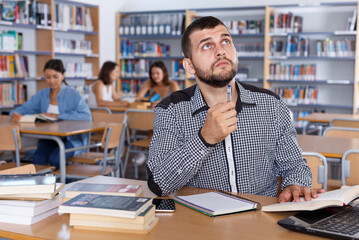 Obraz premium Young focused guy student working with laptop and books in university library