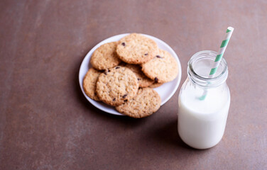 Fresh delicious milk in a glass bottle on a textured background with chocolate cookies on a white plate.