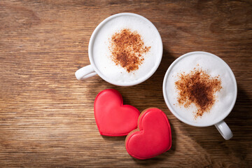 Valentines day.  Cups of cappuccino coffee and colorful heart shaped cookies on wooden background