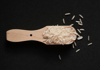Basmati rice in wooden scoop on black background.