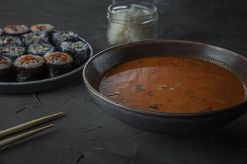 a bowl of soup tom yam. Set of sushi and a jar of rice on the background
