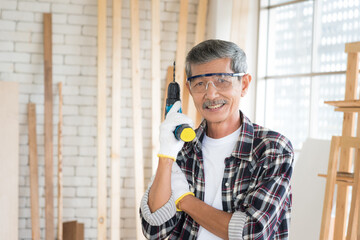 Fototapeta na wymiar Portrait senior asian old man holding electric screwdriver with smile emotion in carpenter workshop