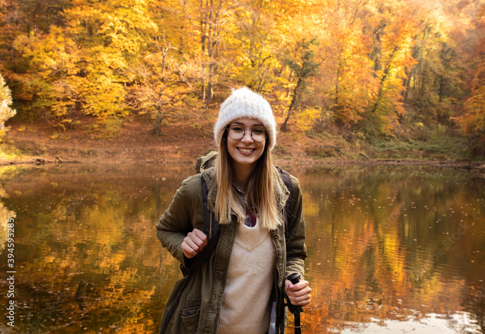 Wall mural Portrait of young female hiker with backpack standing in forest by the lake.