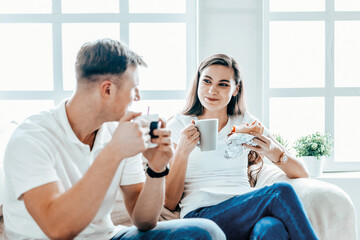 young couple drinks coffee sitting on the sofa in a new apartment.